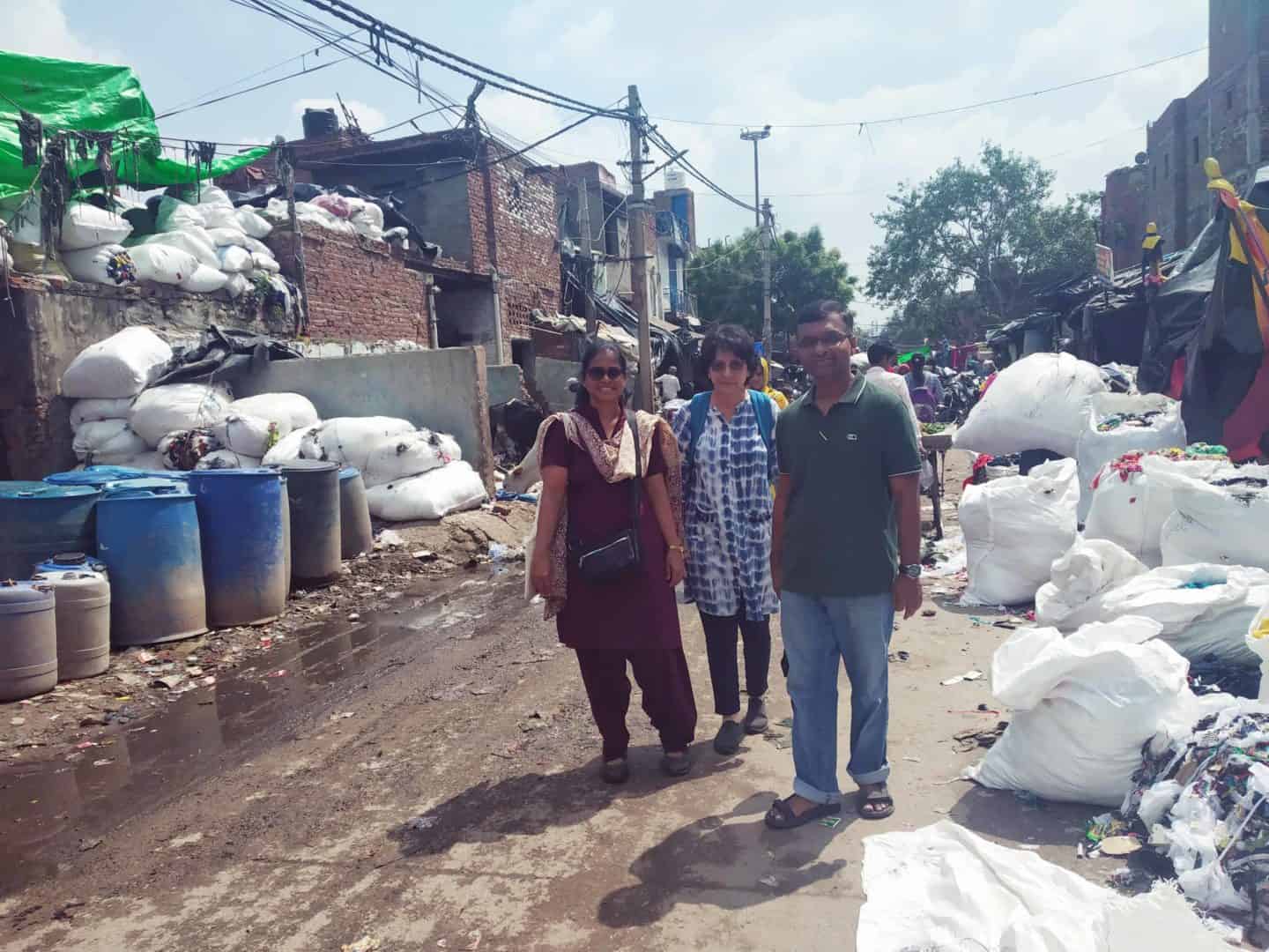 Three people standing in the middle of a dirty urban road, lined with trash on both sides