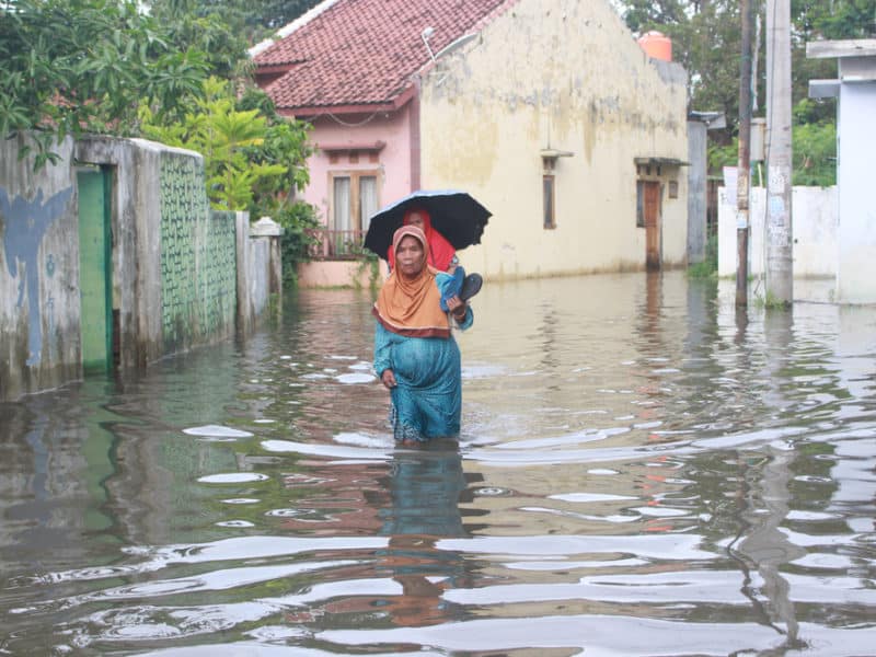 Woman walking through flood water in Indonesia, carrying a child on her back
