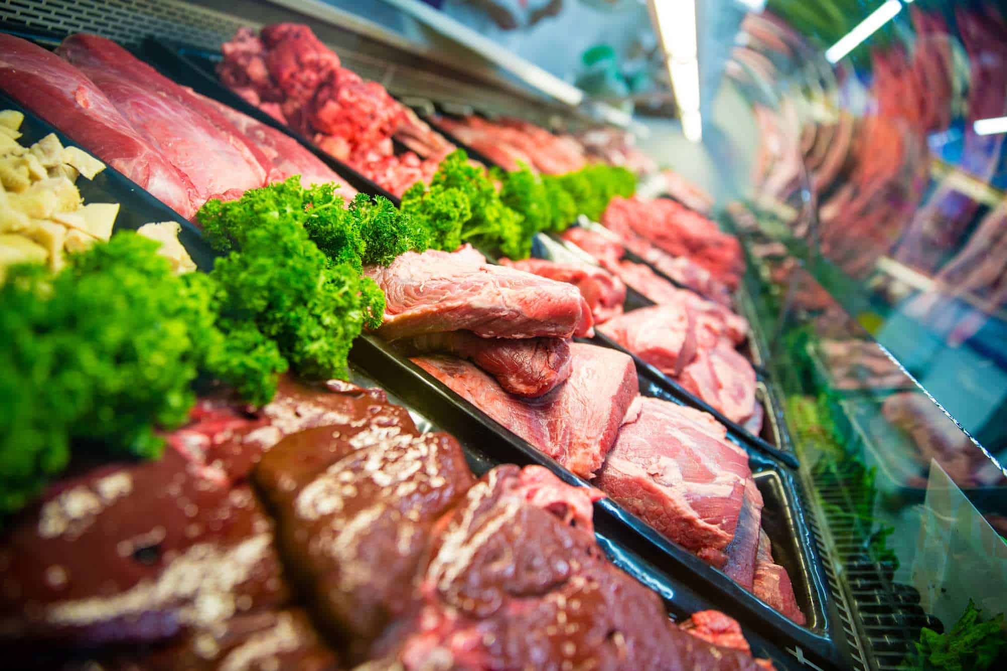 A glass butcher showcase of red meat in a supermarket, with each type of cut separated by parsley.
